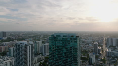 Fly-over-modern-high-rise-building-in-city.-Revealing-panoramic-view-of-residential-urban-borough-at-sunset.-Miami,-USA