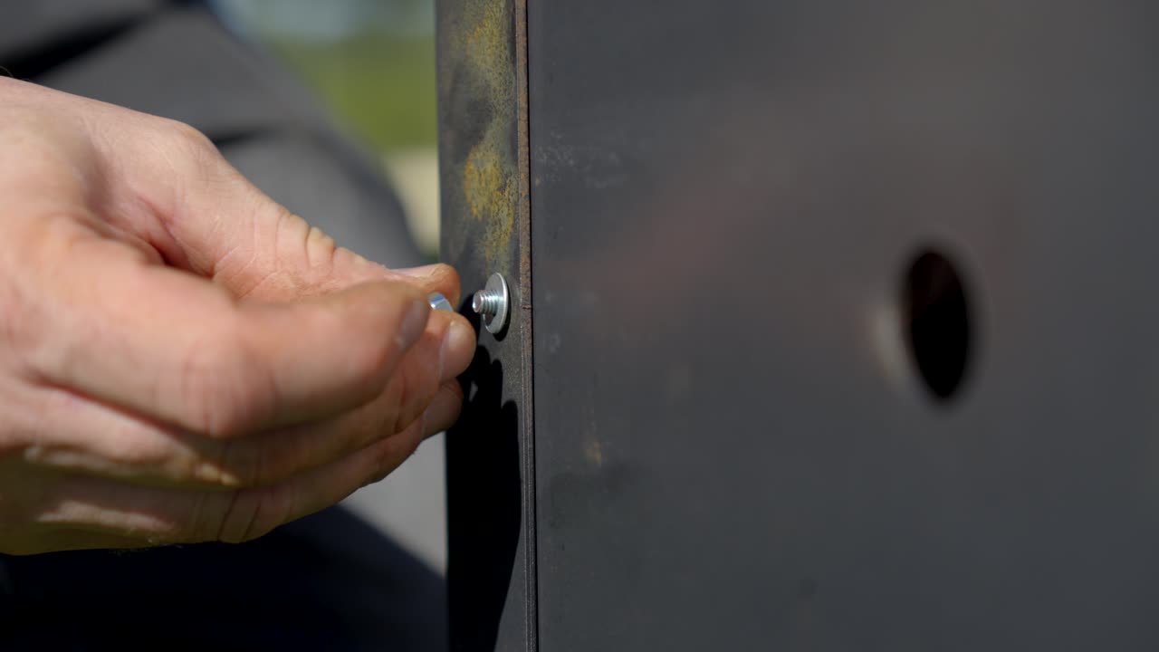 Primo piano di una mano che stringe una vite metallica su un pannello industriale durante lavori di installazione all'aperto