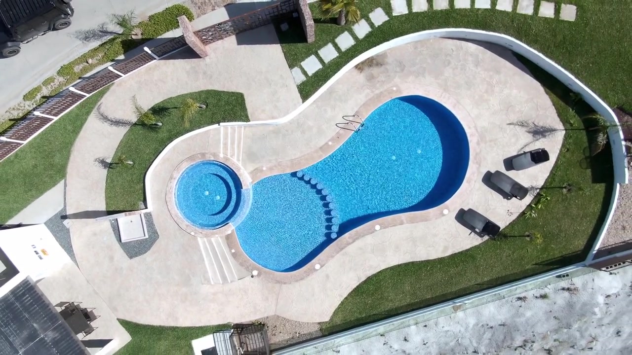Top-down droneudsigt fra luften af en blå swimmingpooloverflade med cirkulære indgangstrin, geometriske mønstre og klare vandteksturer i rekreative omgivelser