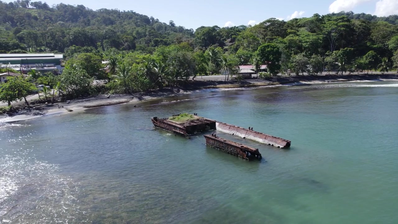 プエルトビエホの緑豊かな熱帯の海岸線近く、浅いターコイズブルーの海に横たわる打ち捨てられた錆びた船