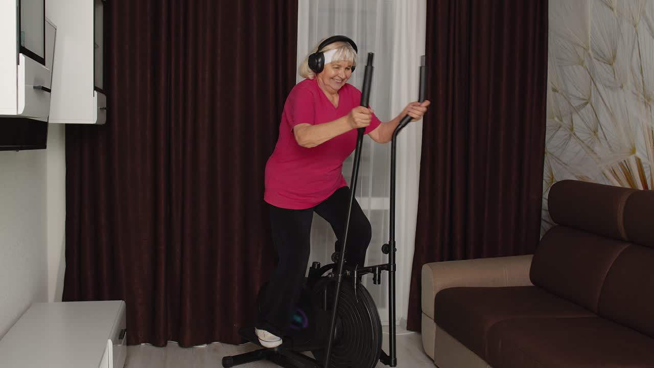 코로나바이러스 봉쇄 기간 동안 집에서 객실에서 피트니스 운동을 하는 오비트렉을 사용하는 고령 여성