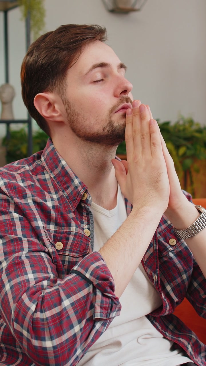 Jovem tenso, com as mãos postas, orando a Deus, pedindo ajuda, sentindo-se estressado e parecendo desesperado.
