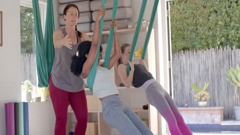 diverse fitness teenage girls in aerial yoga class with female coach in big white room, slow motion