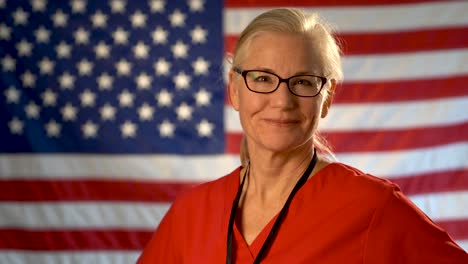 medium tight portrait of a healthcare nurse turning her head and smiling with out of focus american flag