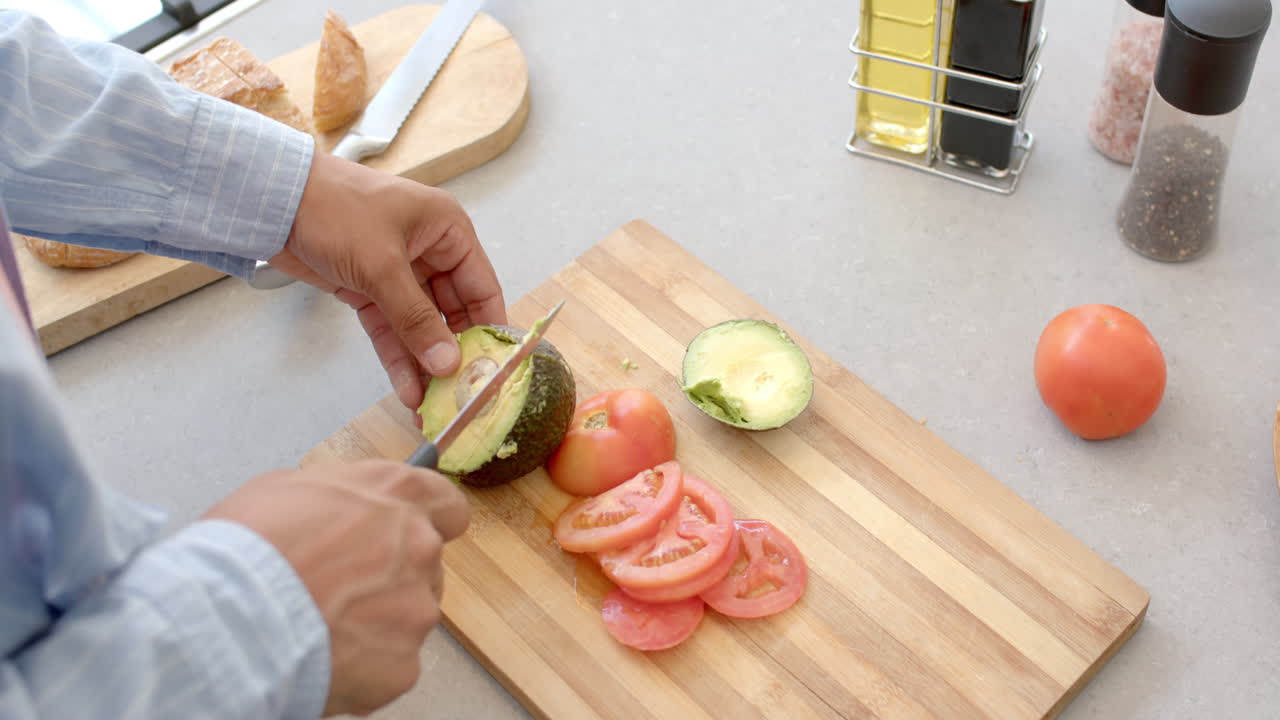 Slicing avocado and tomatoes on cutting board, person preparing fresh ingredients