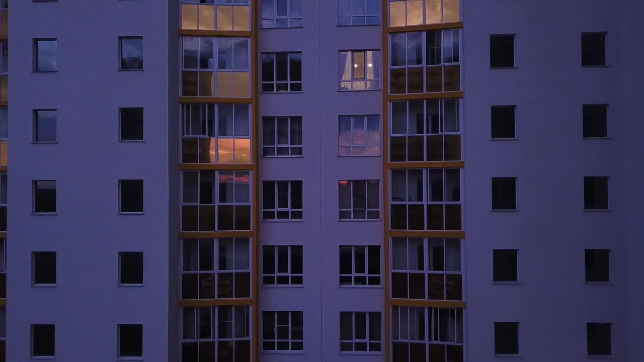 Drone view of colorful facade contemporary apartment building, windows and balconies. Aerial footage highrise estate at night time.