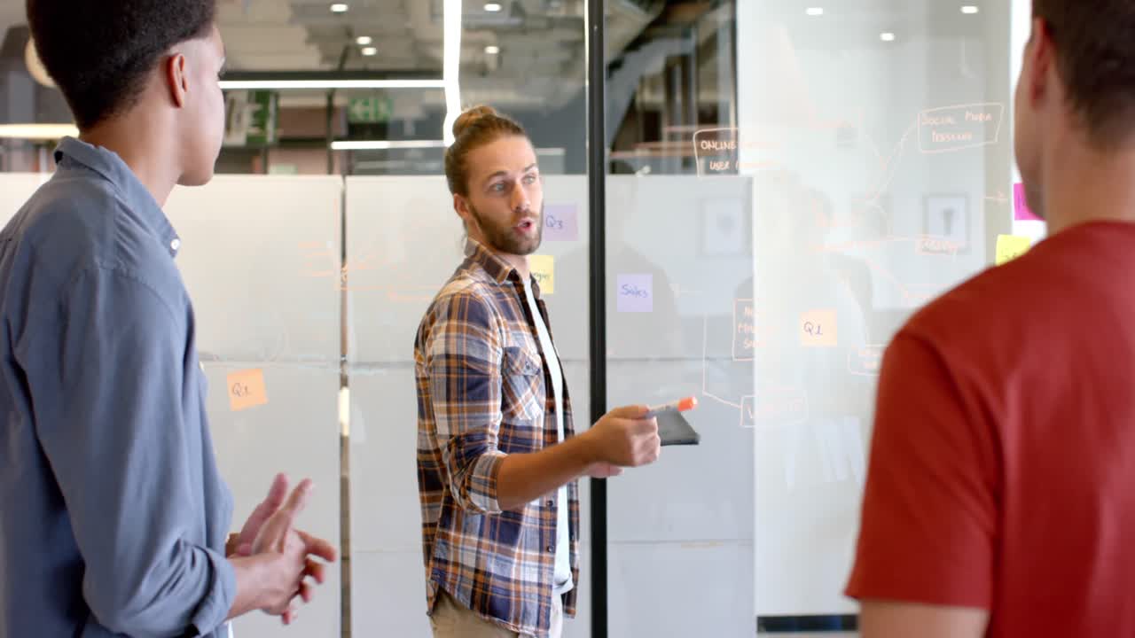 Happy caucasian casual businessman presenting to diverse colleagues at glass wall, slow motion
