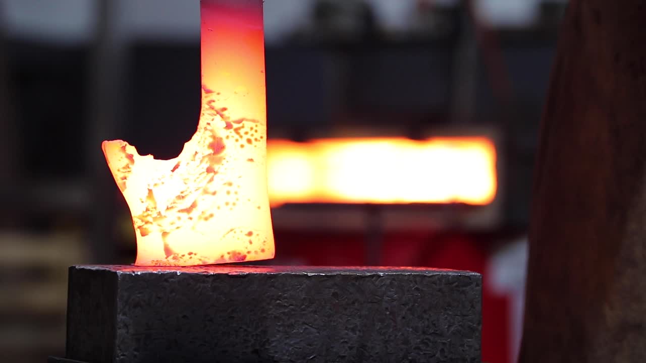 Blacksmiths forging hot metal with hammer in workshop