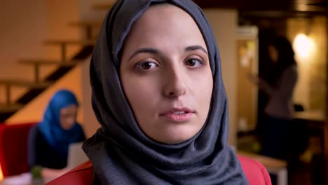 closeup portrait of young attractive arabian female office worker in gray hijab turning from the side to camera and looking straight