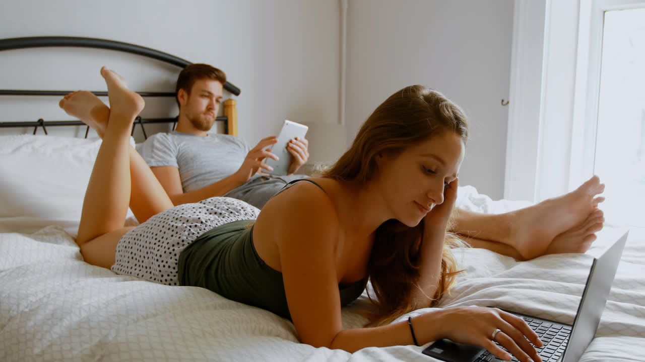 Couple using laptop and digital tablet on bed 4k 