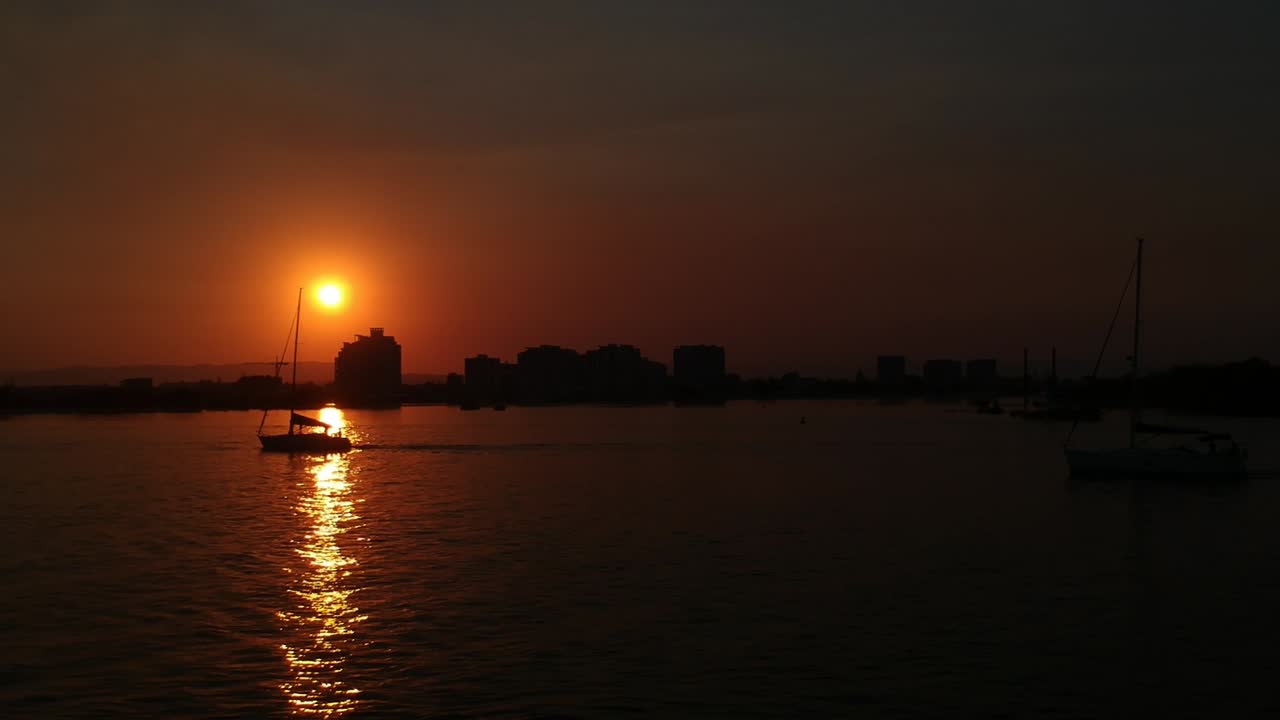 Auringonlaskun purjeveneet ja kaupungin siluetti