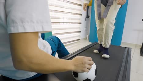 low angle view of a young patient during physical rehabilitation as the patient kicks a soccer ball on a treadmill to improve balance and coordination