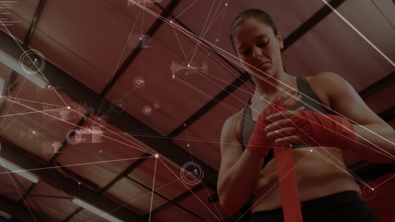 Female athlete wrapping red boxing hand wraps in gym displaying fitness data overlay on metal beams