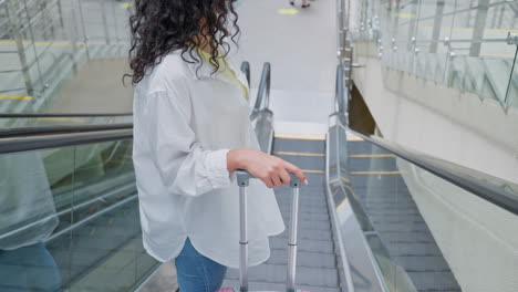 mujer con equipaje en una escalera mecánica del aeropuerto
