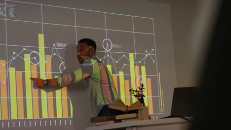 profesor masculino dando una lección de matemáticas o ciencias en la escuela de pie en la parte delantera de la clase con la proyección del gráfico 2