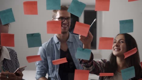 Diverse-Team-Of-Positive-Young-People-Smiling-While-Working-Together-During-Brainstorming-And-Standing-Behind-Glass-Wall-With-Sticky-Colorful-Papers