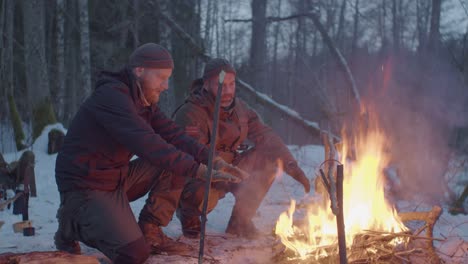 dos hombres cerca de una fogata en un bosque nevado