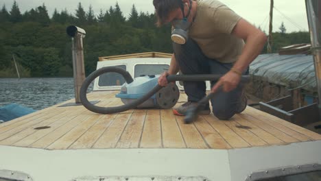 young carpenter hoovering sanded wooden boat roof