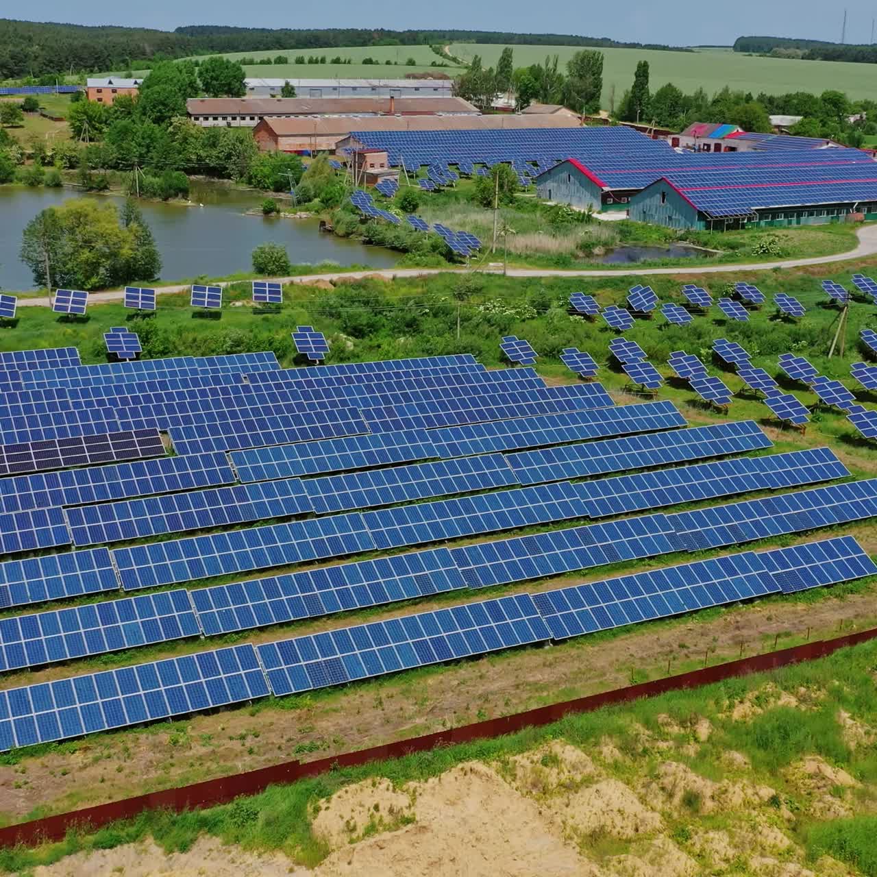 Solar power plant among nature. Photovoltaic panels in the field and roofs of industrial buildings. Renewable clean energy from the sun. Aerial view.