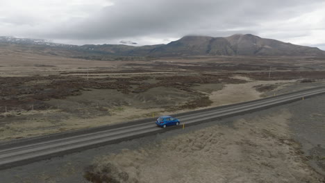 aerial view with close tracking to blue car and over the road leading to the icelandic rock formation of hvitserkur on a dull day