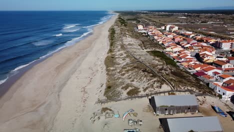 Aerial-orbiting-shot-of-long-sandy-beach,-dunes-and-apartments-with-blue-Atlantic-Ocean-during-sunny-day---Praia-de-Mira,Portugal-in-summer