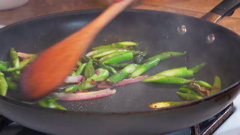 stir-frying asparagus and onions in a pan on the stove with a wooden spoon