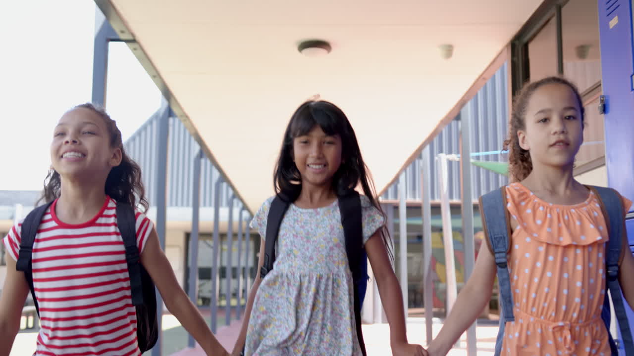 Three biracial girls are walking with backpacks in a school setting