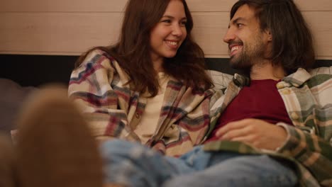 Close-up-shot-of-a-happy-couple,-a-brunette-girl-in-a-pink-plaid-shirt,-together-with-her-brunette-boyfriend-in-a-green-plaid-shirt,-lie-on-shoes-on-the-trailer-sofa-and-communicate-with-each-other-during-their-picnic-outside-the-city-in-a-camp-in-the-summer