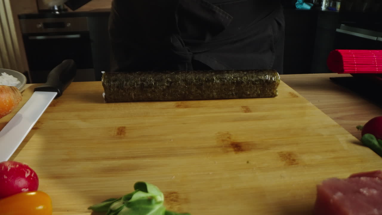 Uno chef prepara e affetta rotoli di sushi su un tagliere di legno