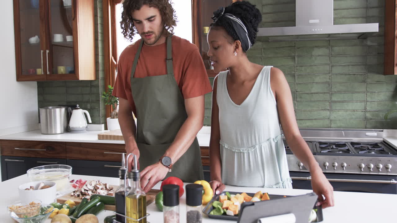 Giovane donna afroamericana e uomo caucasico che cucinano insieme a casa.