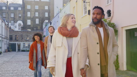 multi-cultural group of friends hugging as they walk along cobbled mews street on visit to city in autumn or winter - shot in slow motion