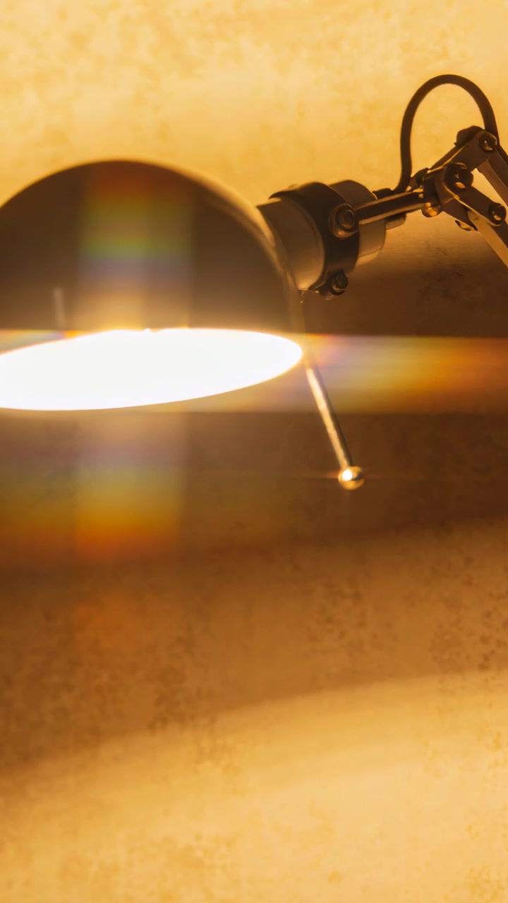 Video vertical: Siguiendo el ligero movimiento de una lámpara de escritorio de metal que proyecta luz cálida sobre una cadena en la pared que se desplaza.