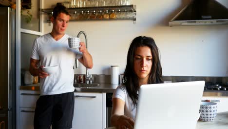 Woman-using-laptop-while-man-drinking-coffee-in-kitchen