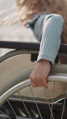 hands of little girl with loose curly hair spinning large wheels of medical vehicle. child with disability learns to move in wheelchair on street closeup