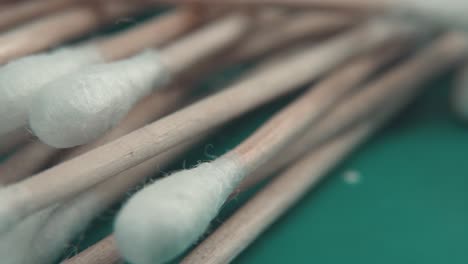 Una-Suave-Panorámica-Macro-Detallada-A-La-Derecha-De-Un-Montón-De-Puntas-Q,-Puntas-De-Algodón-Suave-Blanco,-Palos-De-Madera-Marrón,-Iluminación-De-Estudio-Profesional,-Fondo-Verde,-Vídeo-De-4k