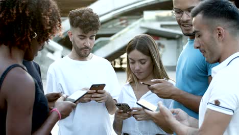 cheerful friends standing in circle on square with phones