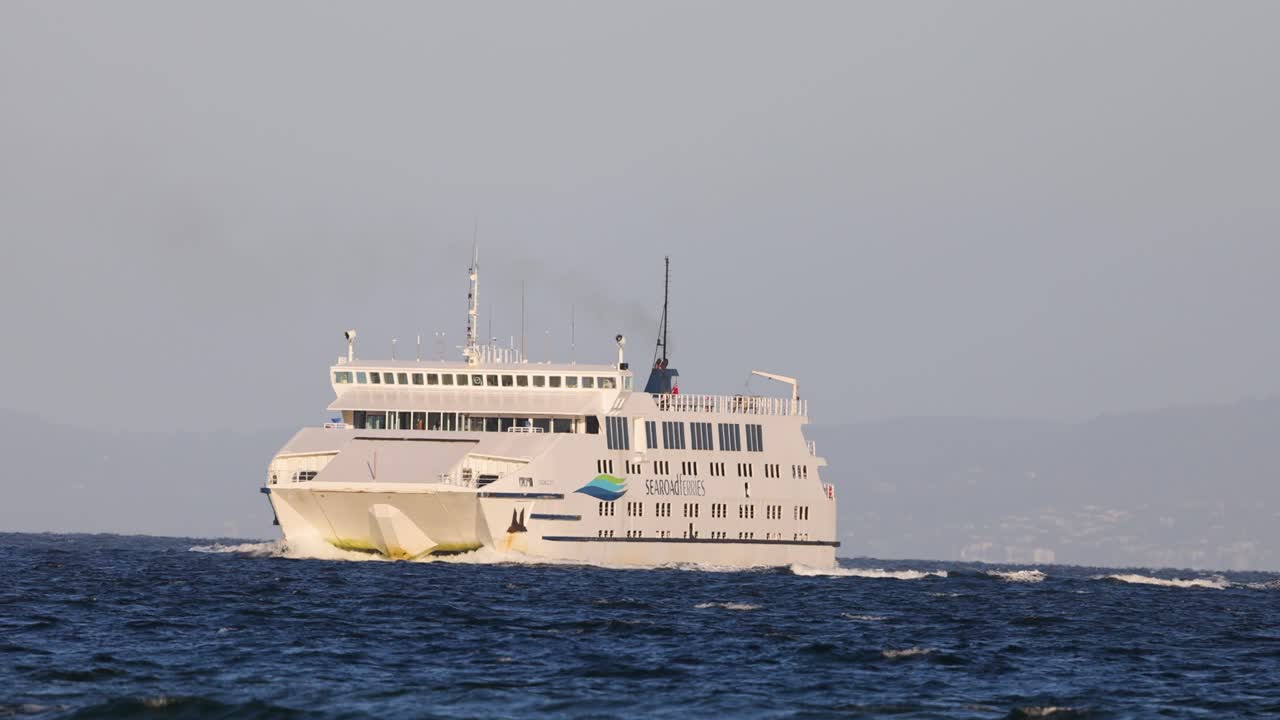 A ferry travels smoothly across the ocean under clear skies, captured in steady daylight with a serene atmosphere