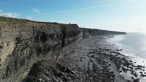 Tracking-drone-shot-over-Welsh-coast-in-the-sunshine-with-cliffs-to-the-left-of-the-frame