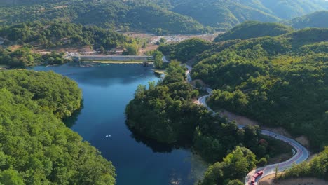 albania's blue eye water spring surrounded by lush green hills and a winding road, aerial view