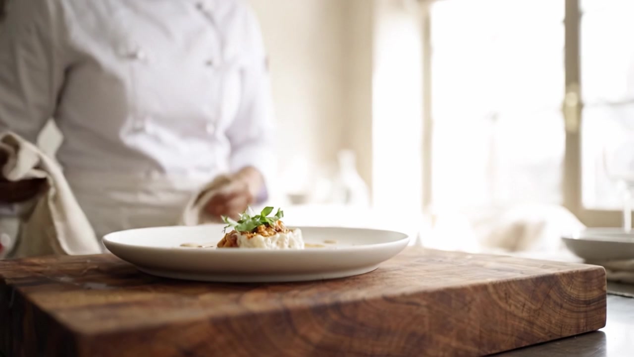A chef meticulously presenting a beautifully plated dish, showcasing culinary artistry and precision in a well-lit kitchen environment.
