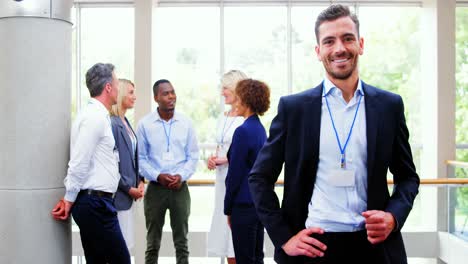 Male-business-executive-smiling-at-camera-while-colleagues-discussing-over-laptop