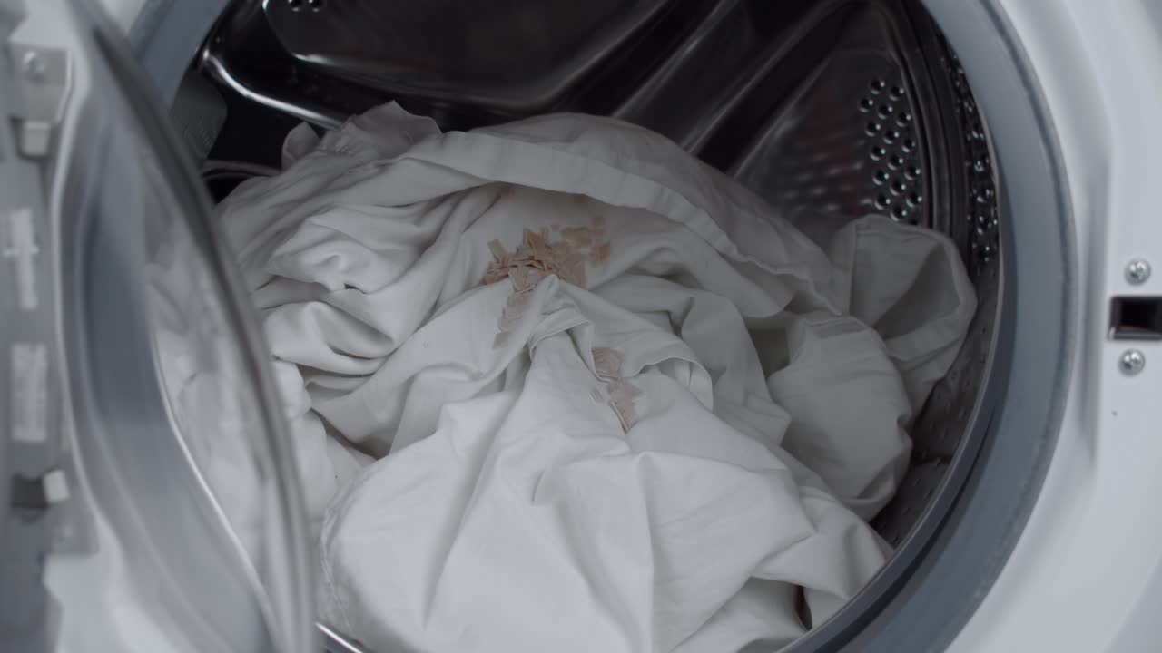 Putting cleaning granules into washing machine drum to wash white cloth, close up slow mo