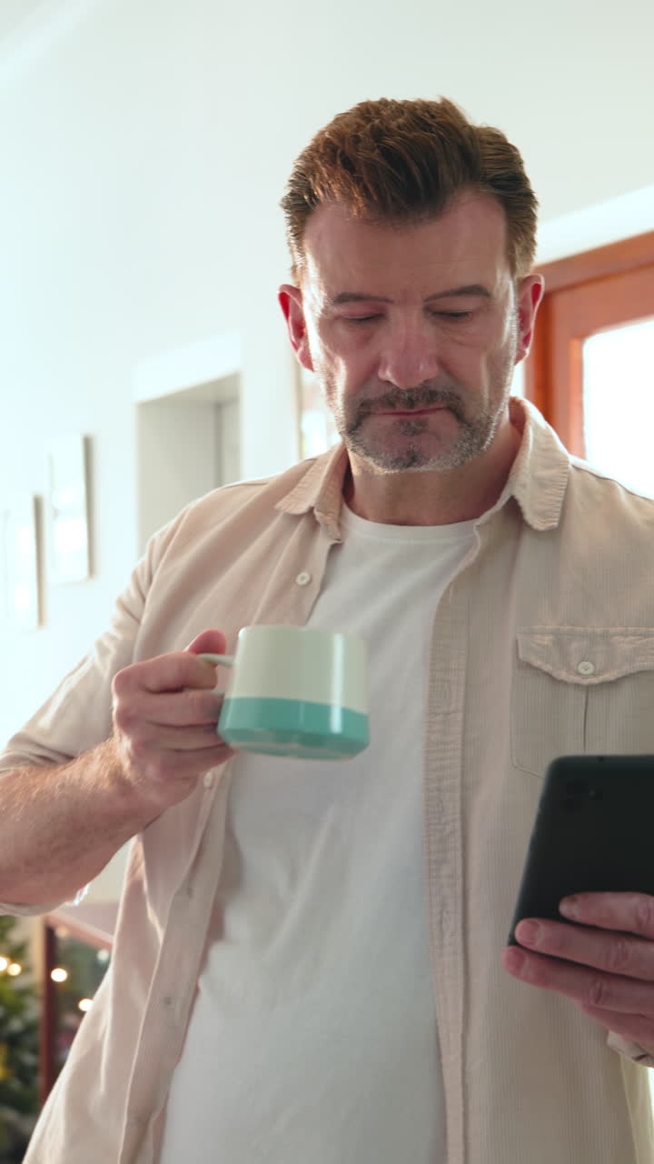Vertical video: Senior man enjoying coffee while reading on smartphone at home