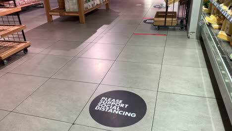 Social-distancing-floor-signage-in-store,-high-panning-shot-from-right-to-left