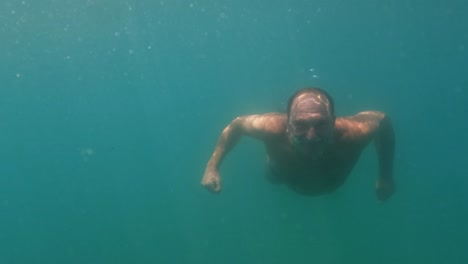 underwater scene of adult man in apnea swimming toward camera while smiling