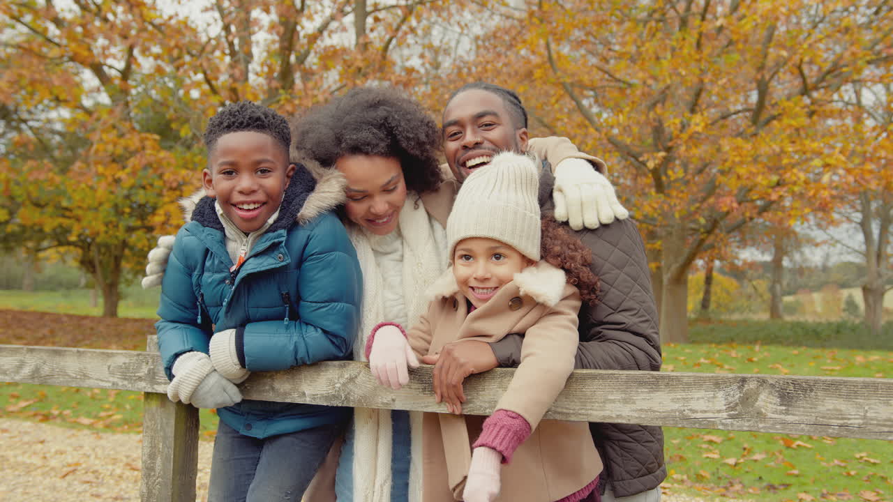 Portrait of smiling family with parents with children leaning on gate on walk through autumn countryside together - shot in slow motion