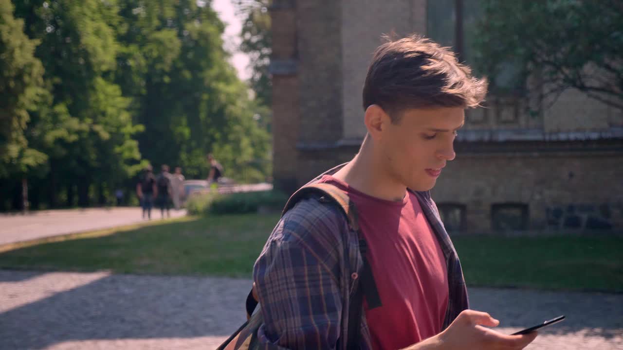 젊은 잘생긴 남자가 여름에 낮에 스마트폰에 프를 고 거리를 고 있습니다.