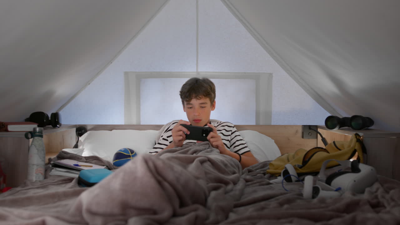 십대 소년 은 지붕 의 침대 에서 휴식 을 하고 휴대 전화 로 놀고 있다