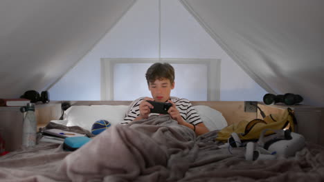 teenager boy relaxing in his loft bed playing on his phone