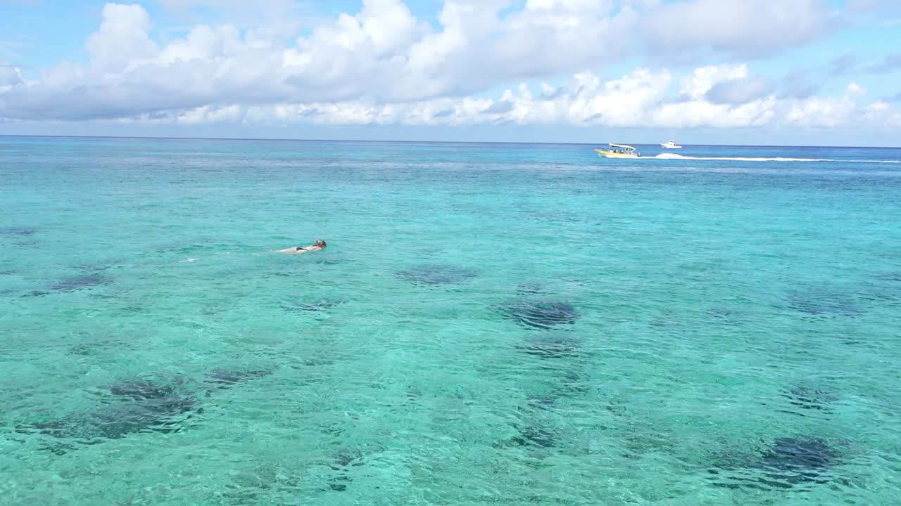 una mujer buceando en las claras aguas tropicales de la isla de cozumel, méxico, mientras una lancha pasa al fondo